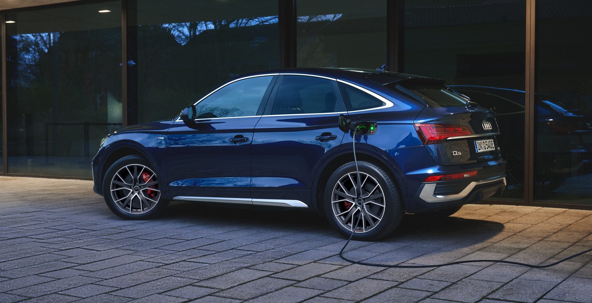 Blue Audi Q5 TFSI plugged in to a charger in a driveway