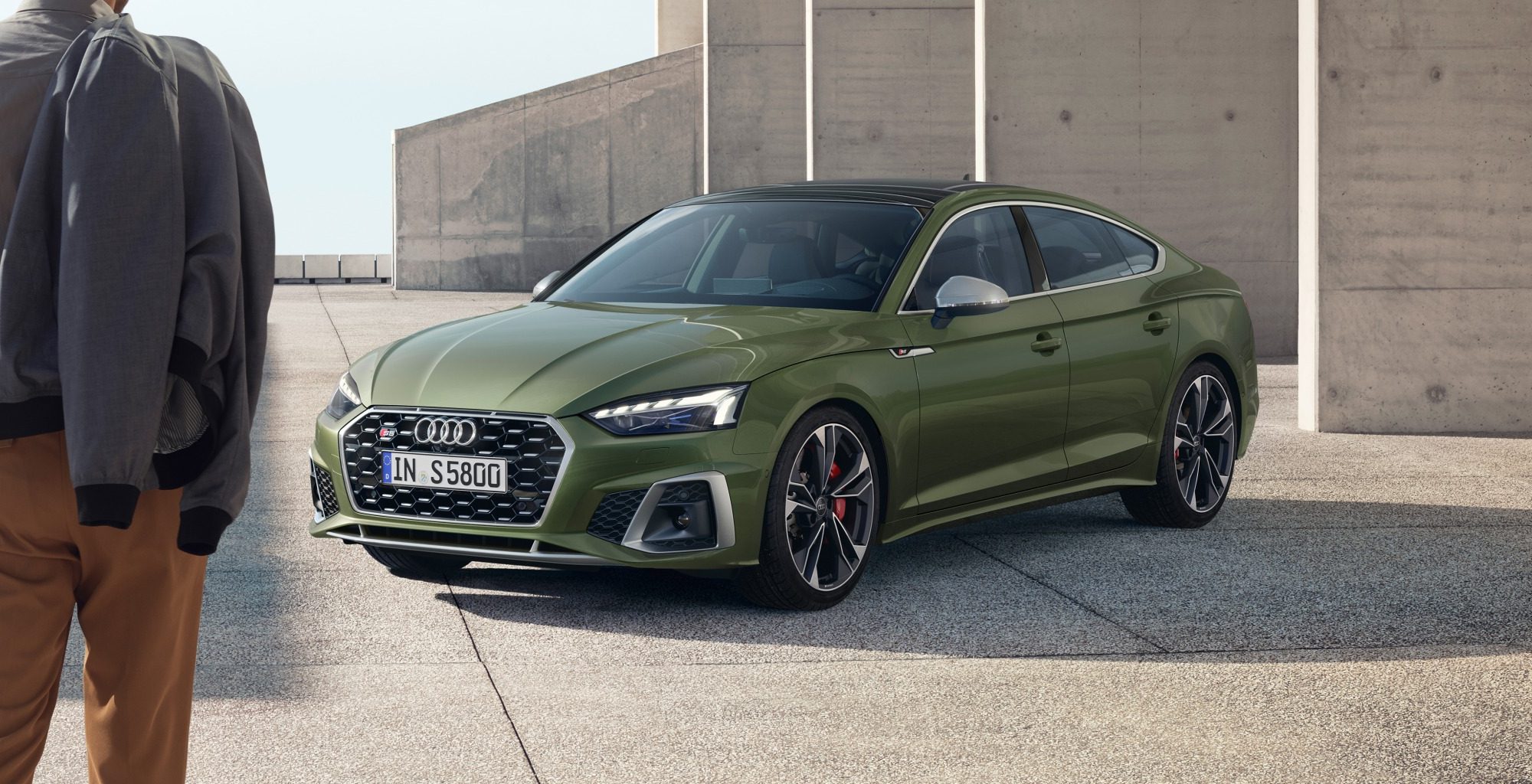 Dark olive green Audi S5 Sportback in an urban setting with a man standing to the side